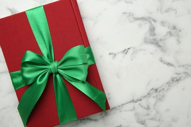 Photo of Book tied with green ribbon on white marble table, top view. Space for text