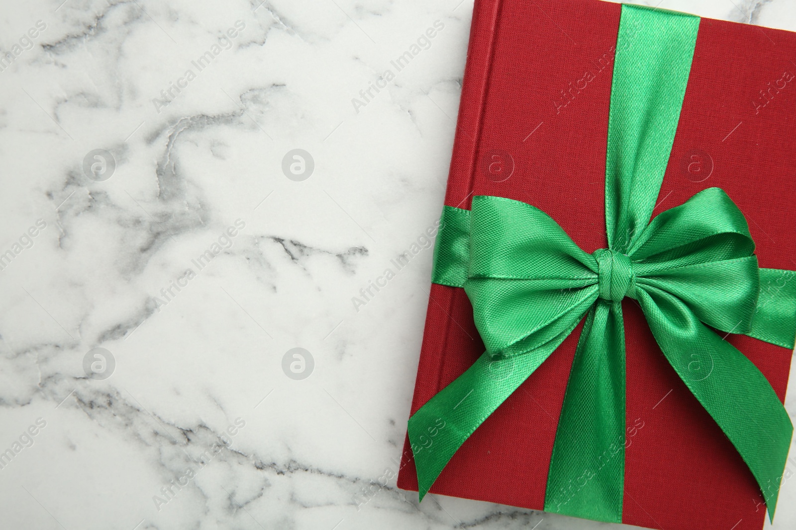 Photo of Book tied with green ribbon on white marble table, top view. Space for text