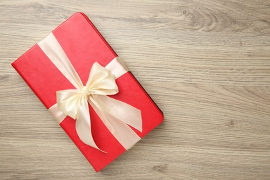 Book tied with beige ribbon on wooden table, top view. Space for text