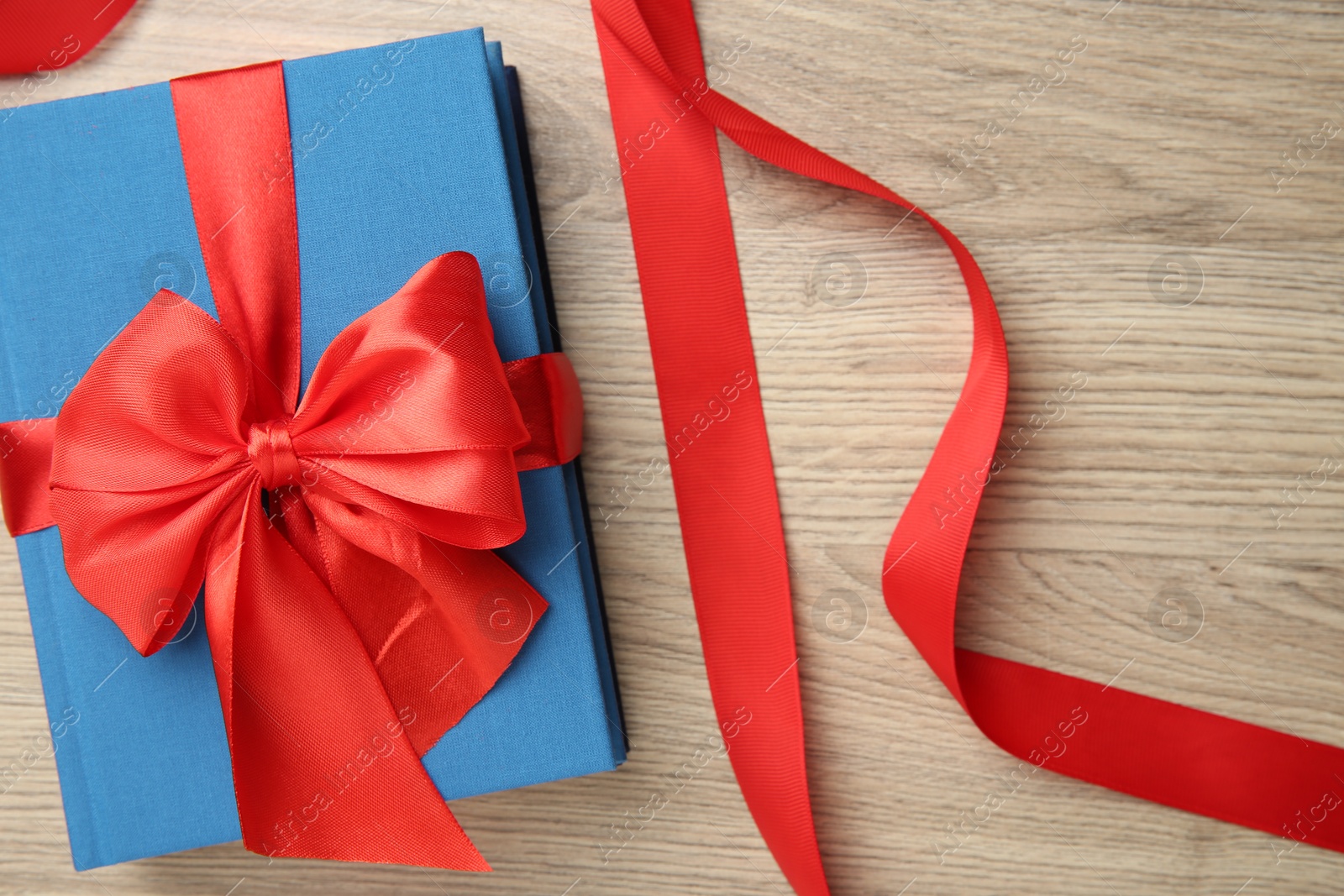 Photo of Book tied with red ribbon on wooden table, top view