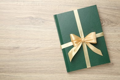 Photo of Book tied with golden ribbon on wooden table, top view. Space for text