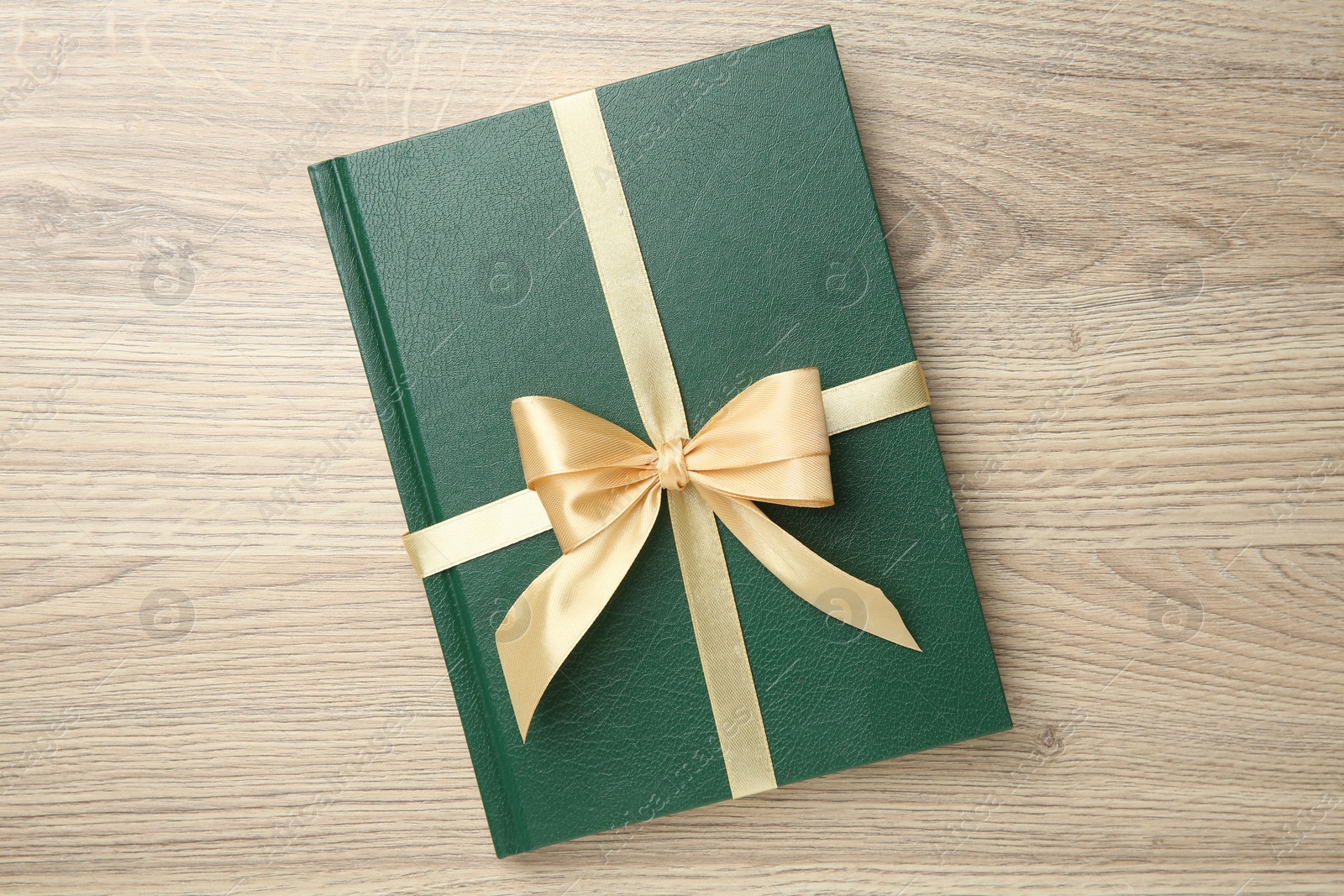 Photo of Book tied with golden ribbon on wooden table, top view