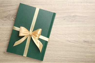 Photo of Book tied with golden ribbon on wooden table, top view. Space for text