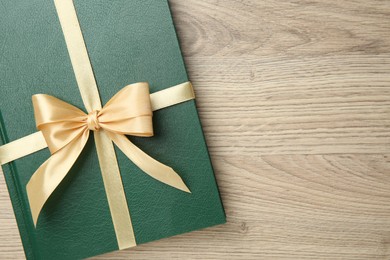 Photo of Book tied with golden ribbon on wooden table, top view. Space for text