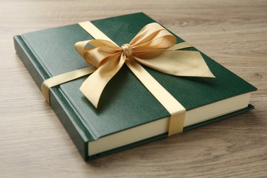 Photo of Book tied with golden ribbon on wooden table, closeup