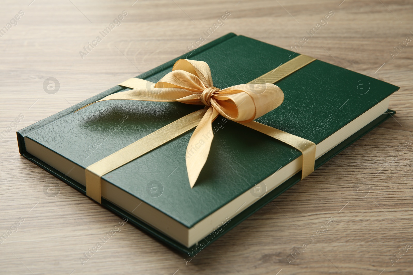 Photo of Book tied with golden ribbon on wooden table, closeup