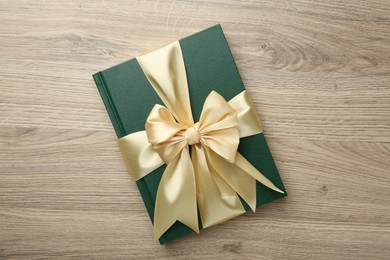 Photo of Book tied with golden ribbon on wooden table, top view