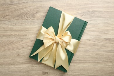 Photo of Book tied with golden ribbon on wooden table, top view