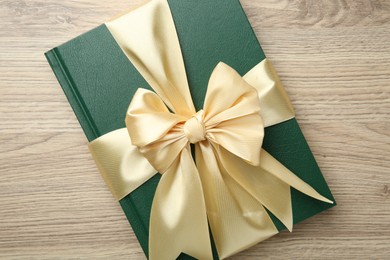 Photo of Book tied with golden ribbon on wooden table, top view