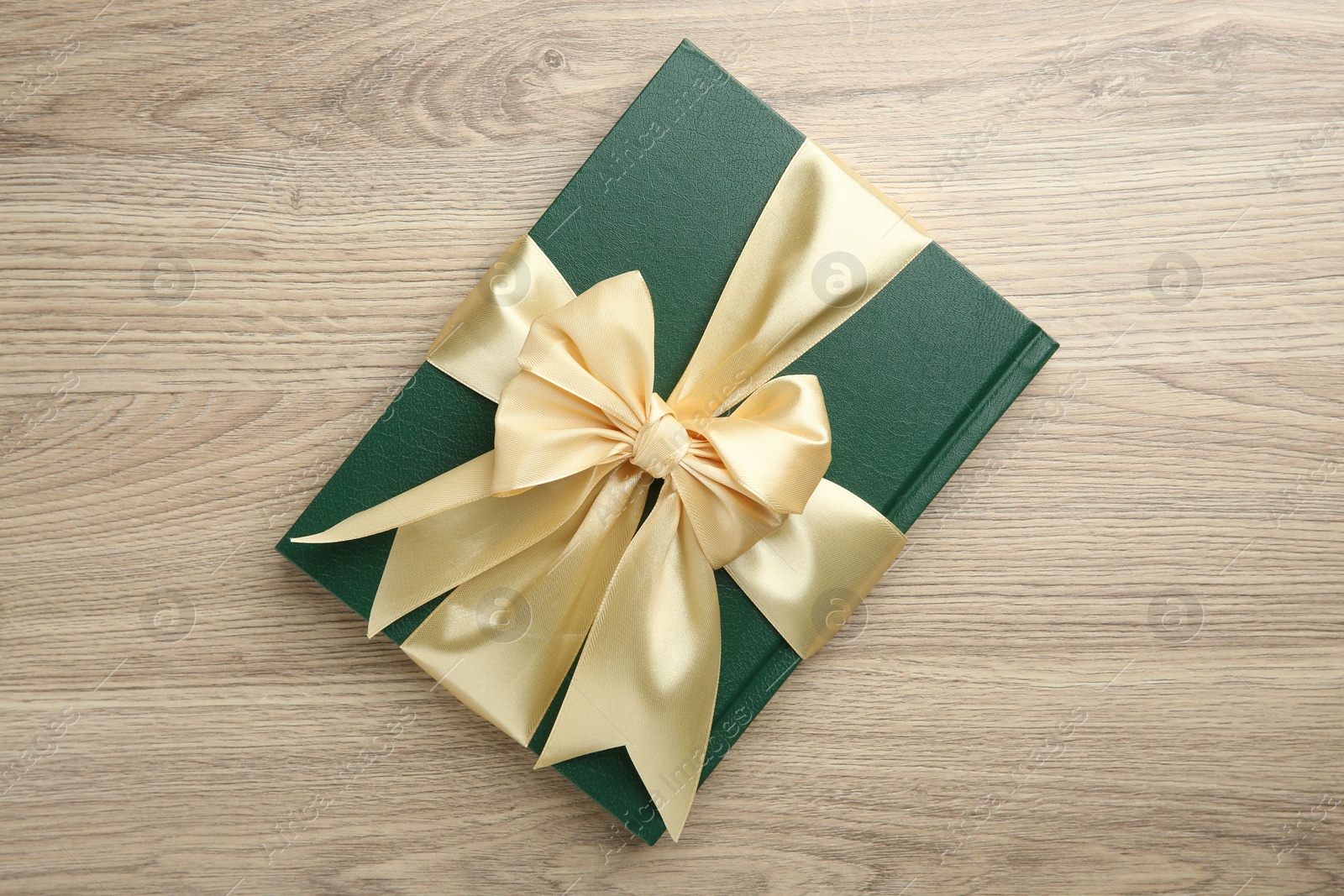 Photo of Book tied with golden ribbon on wooden table, top view