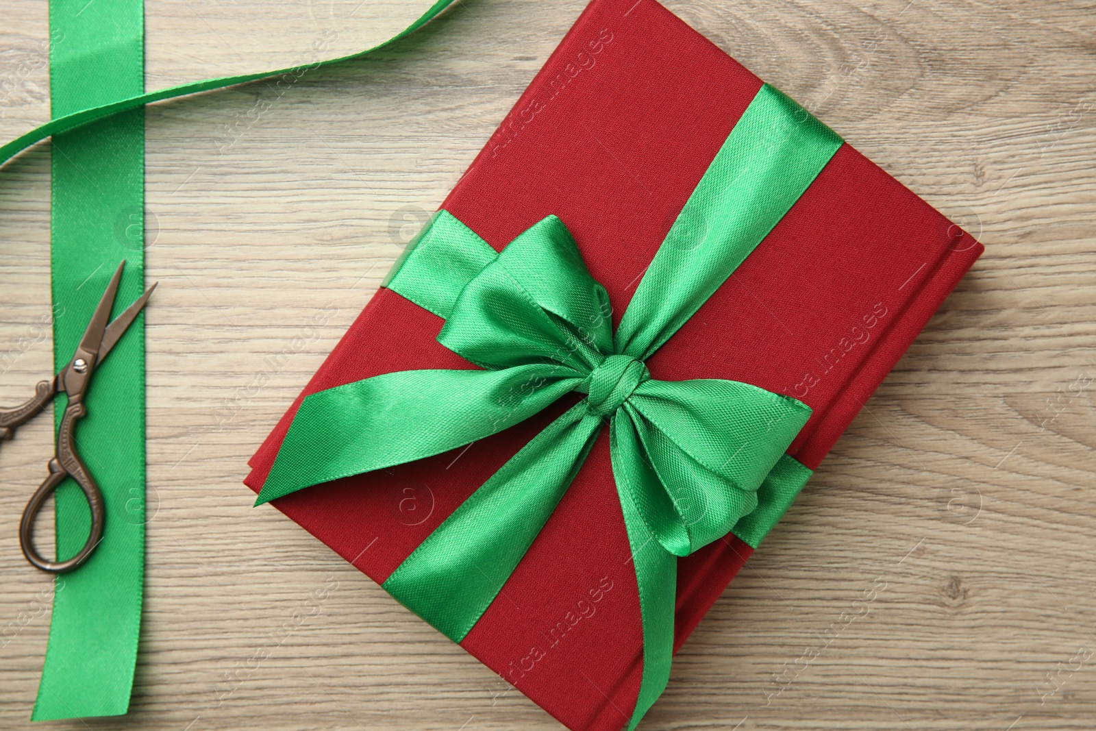 Photo of Book tied with green ribbon and scissors on wooden table, top view