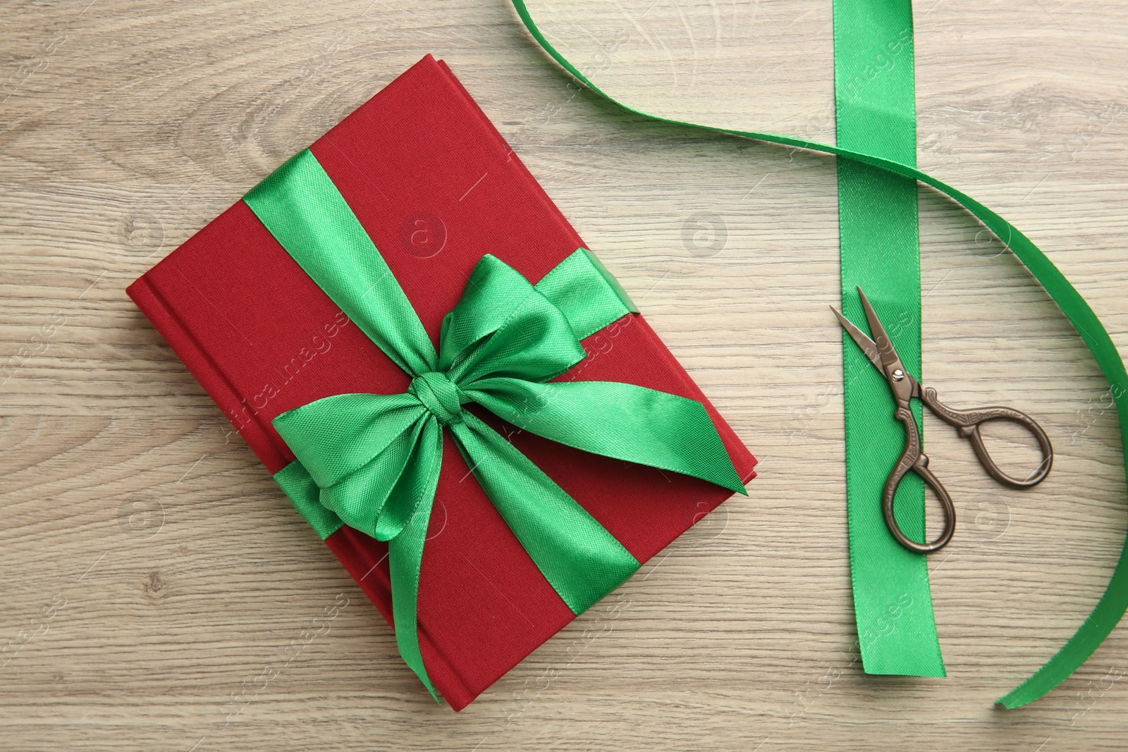 Photo of Book tied with green ribbon and scissors on wooden table, top view