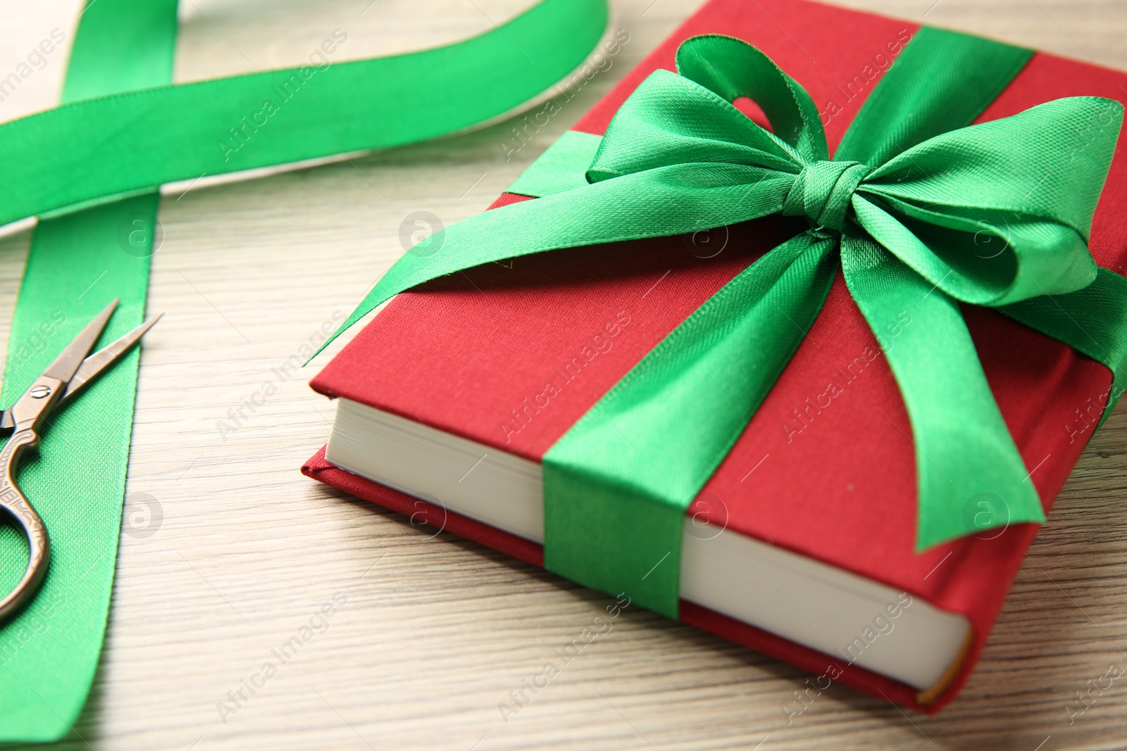 Photo of Book tied with green ribbon and scissors on wooden table, closeup