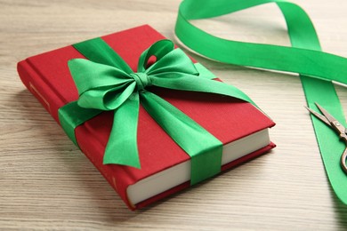 Photo of Book tied with green ribbon and scissors on wooden table, closeup