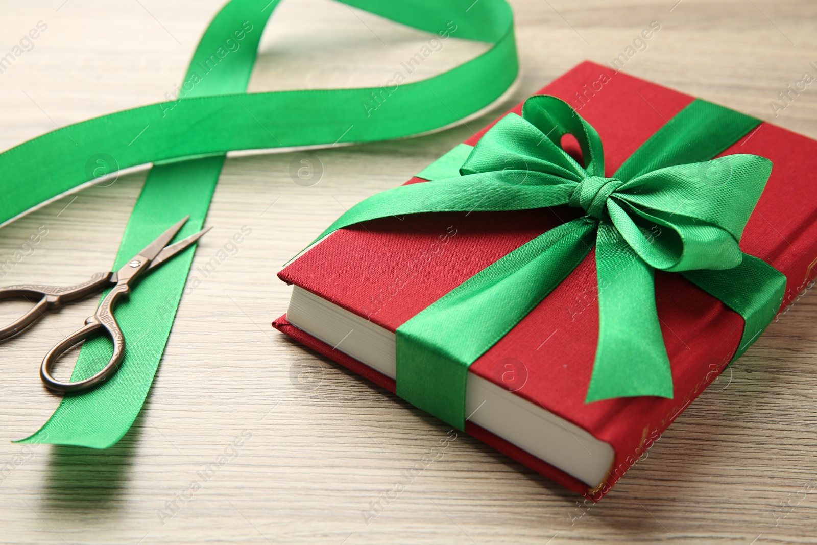 Photo of Book tied with green ribbon and scissors on wooden table, closeup