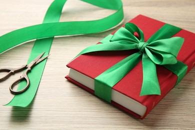 Photo of Book tied with green ribbon and scissors on wooden table, closeup