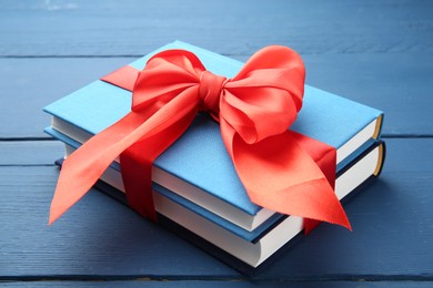 Photo of Books tied with red ribbon on blue wooden table, closeup