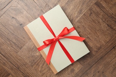 Photo of Hardcover book with ribbon as gift on wooden table, top view