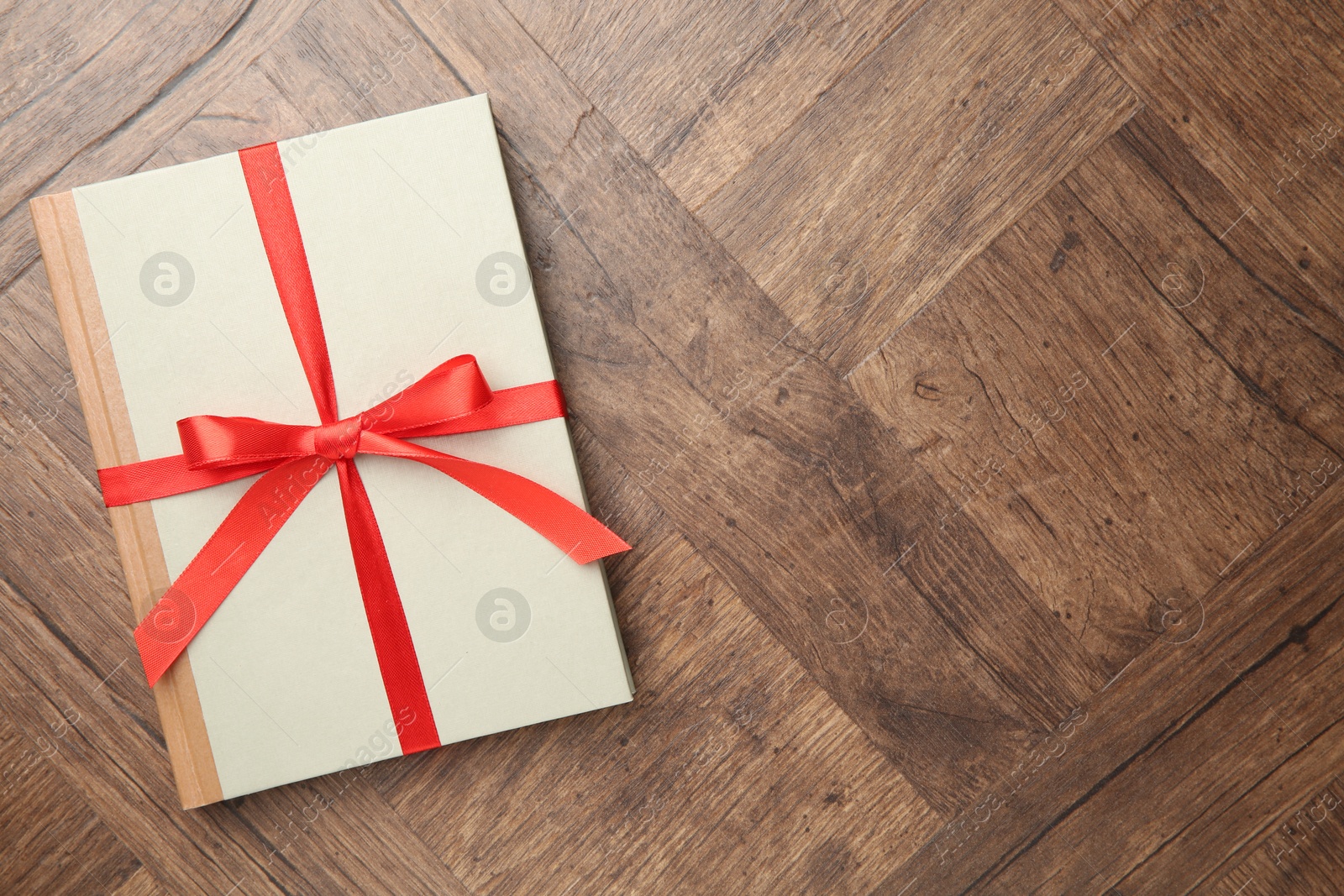 Photo of Hardcover book with ribbon as gift on wooden table, top view. Space for text