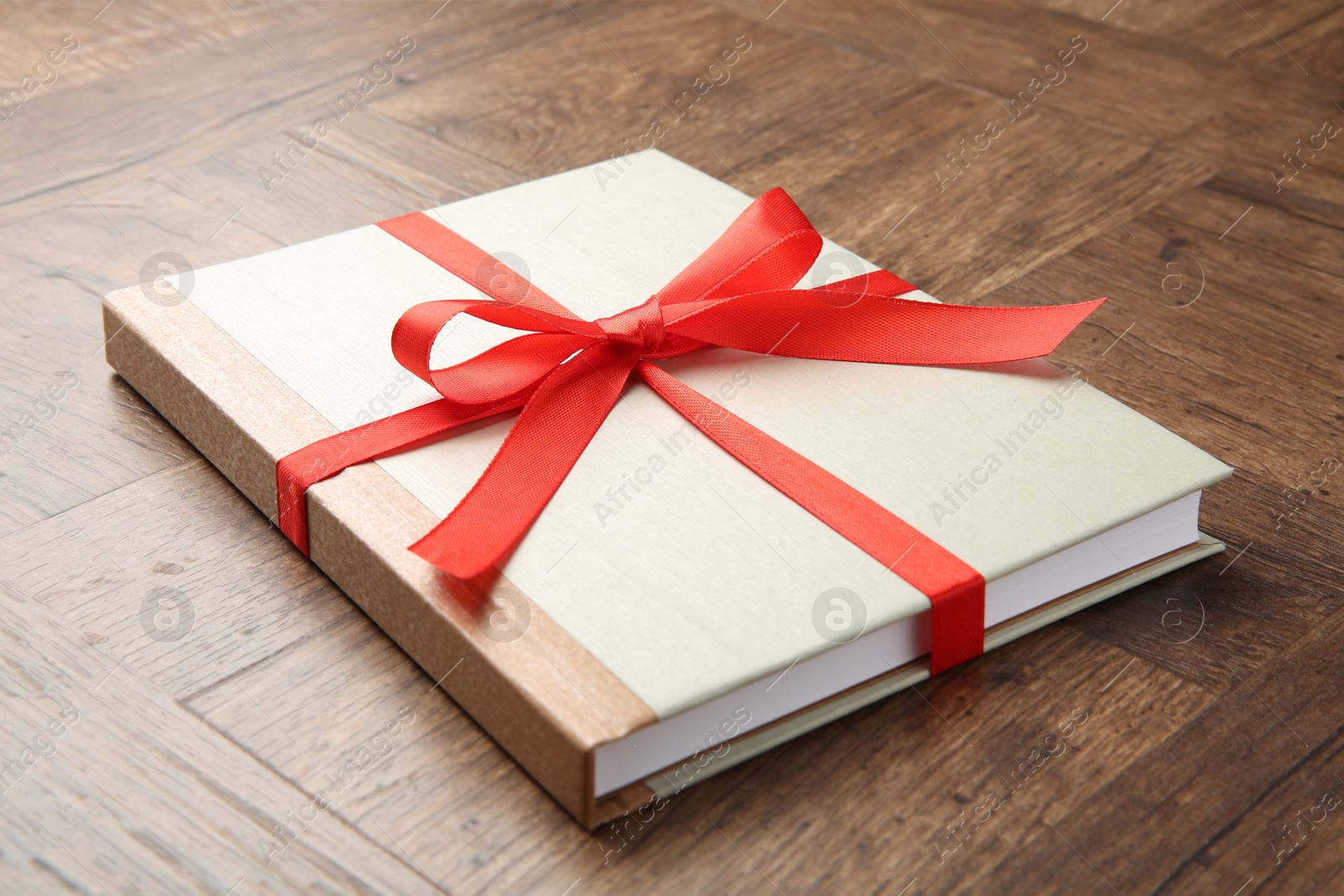 Photo of Hardcover book with ribbon as gift on wooden table