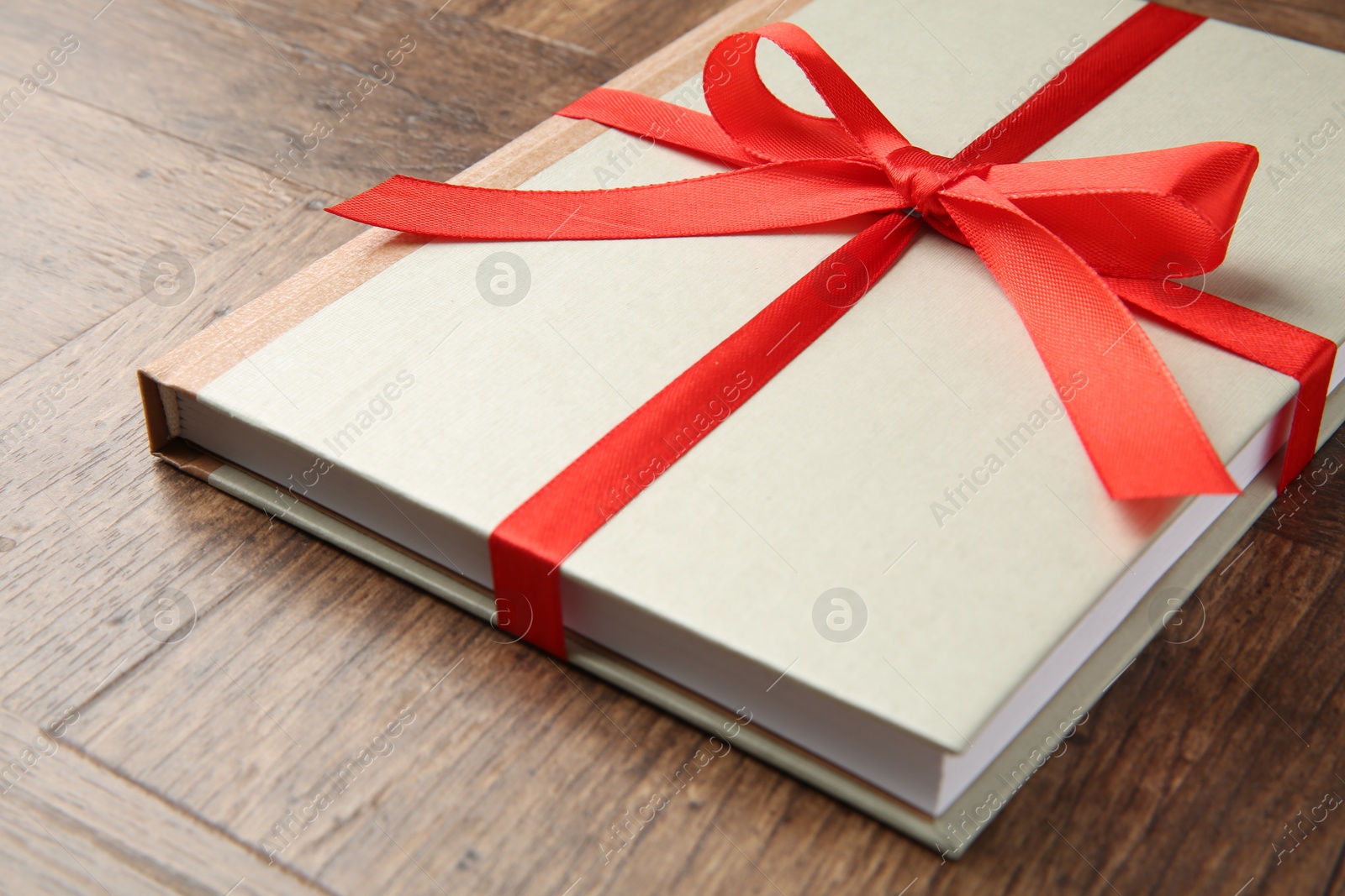 Photo of Hardcover book with ribbon as gift on wooden table, closeup