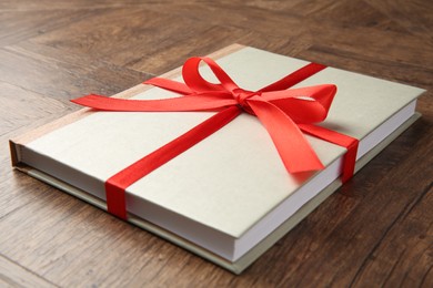 Photo of Hardcover book with ribbon as gift on wooden table, closeup