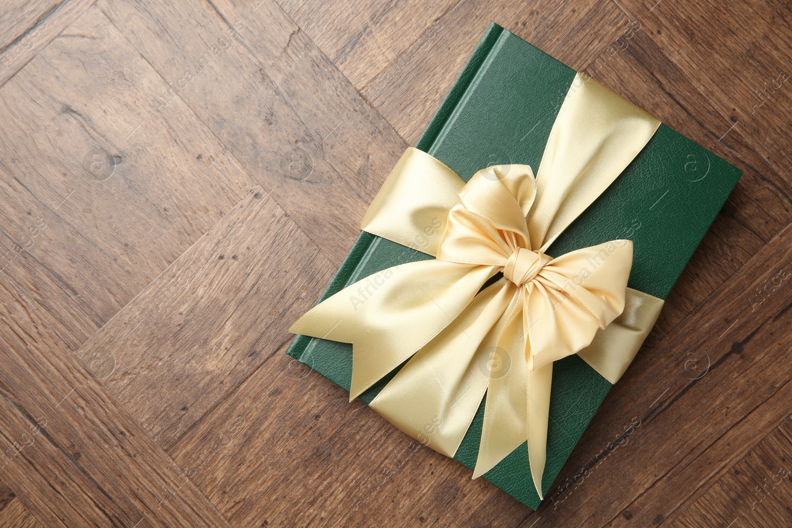 Photo of Hardcover book with ribbon as gift on wooden table, top view. Space for text