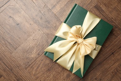 Photo of Hardcover book with ribbon as gift on wooden table, top view. Space for text