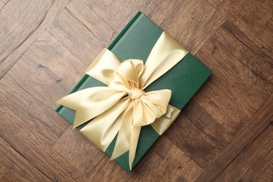 Photo of Hardcover book with ribbon as gift on wooden table, top view