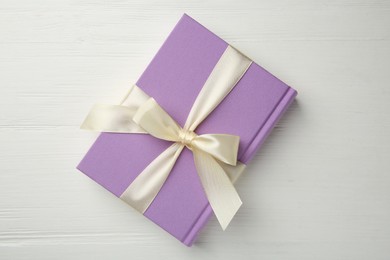 Photo of Hardcover book with ribbon as gift on white wooden table, top view