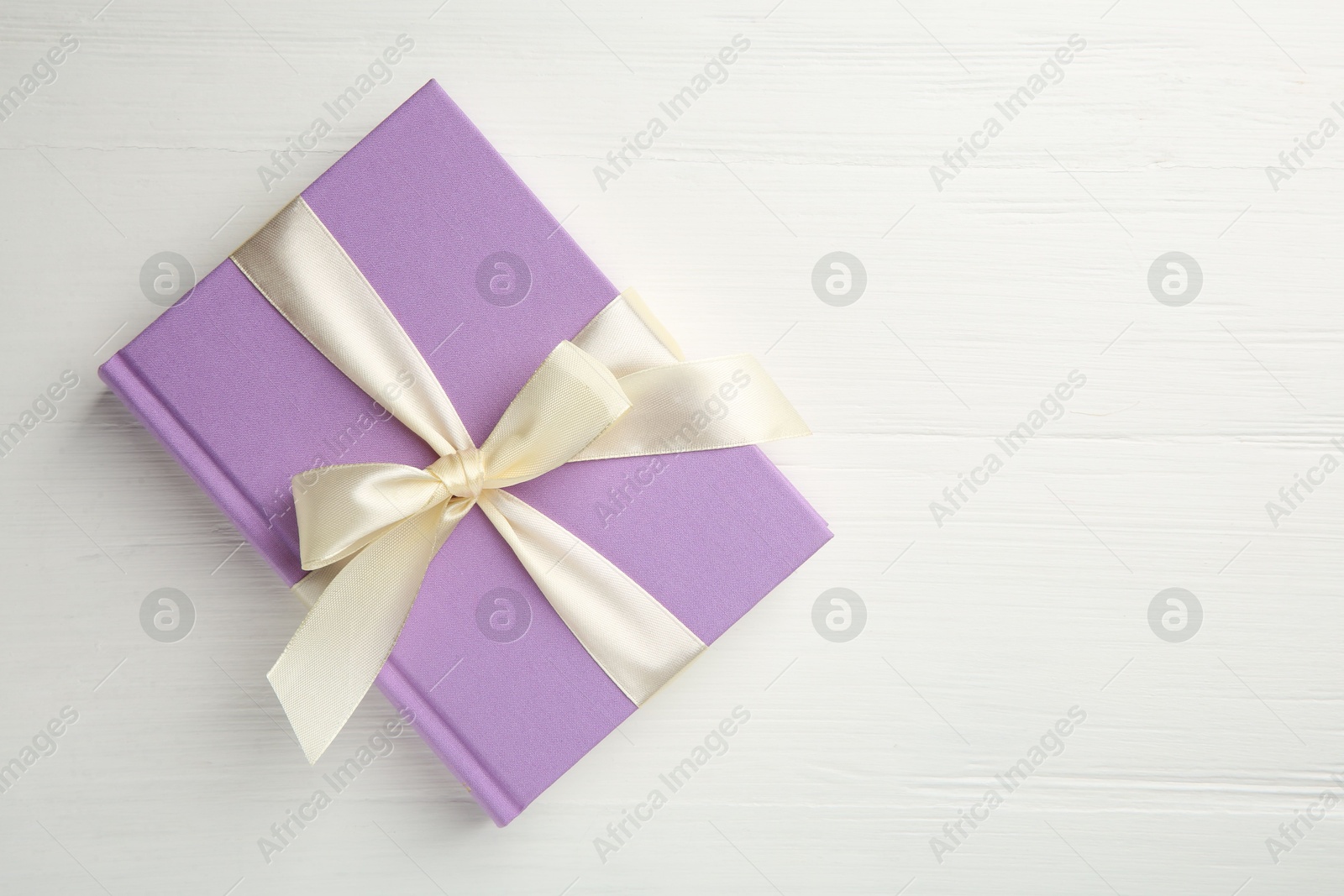 Photo of Hardcover book with ribbon as gift on white wooden table, top view. Space for text