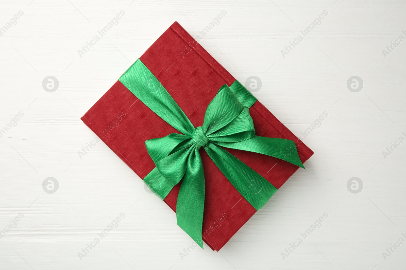 Photo of Hardcover book with ribbon as gift on white wooden table, top view