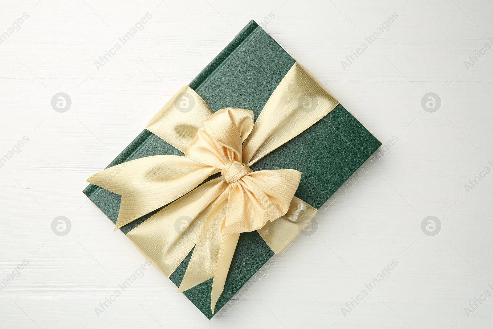 Photo of Hardcover book with ribbon as gift on white wooden table, top view