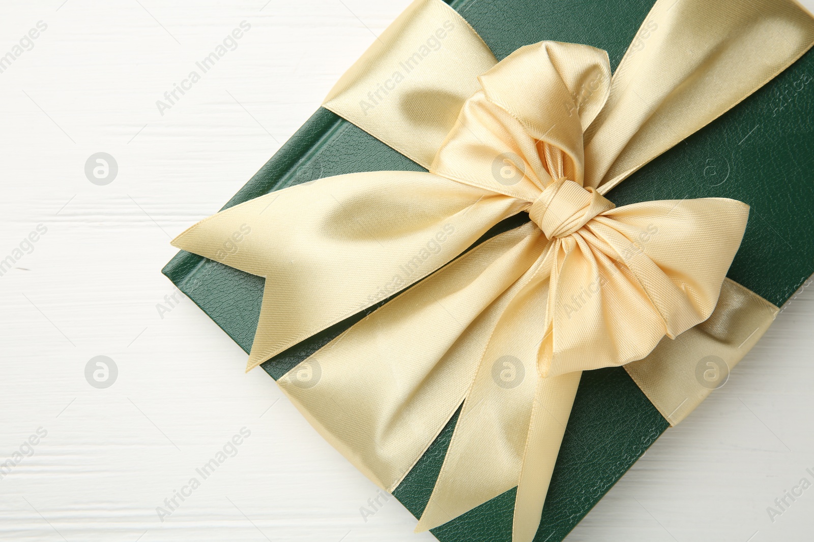 Photo of Hardcover book with ribbon as gift on white wooden table, top view