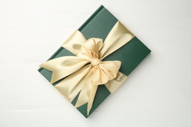 Hardcover book with ribbon as gift on white wooden table, top view