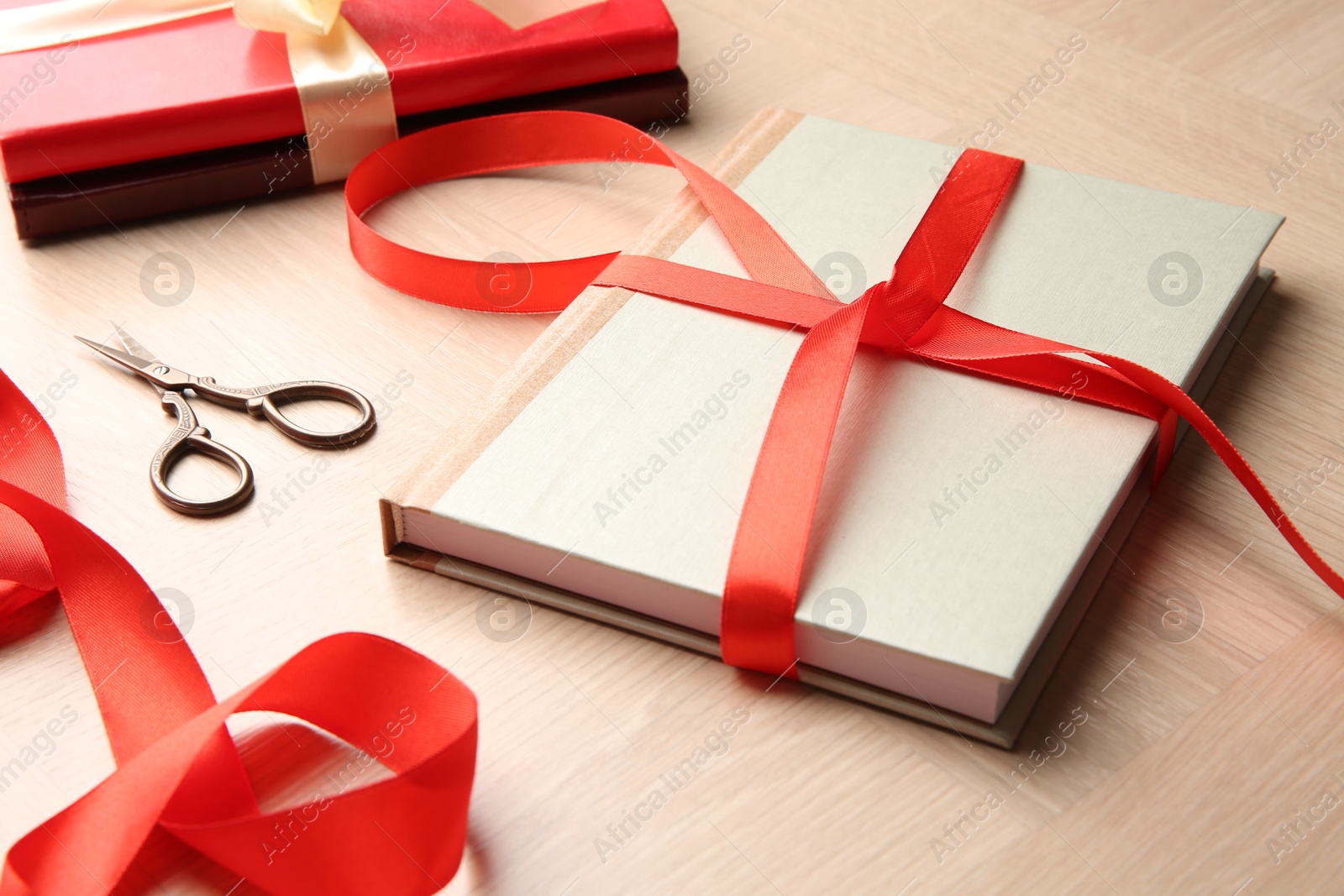 Photo of Hardcover books, ribbon and scissors on wooden table. Preparing gift