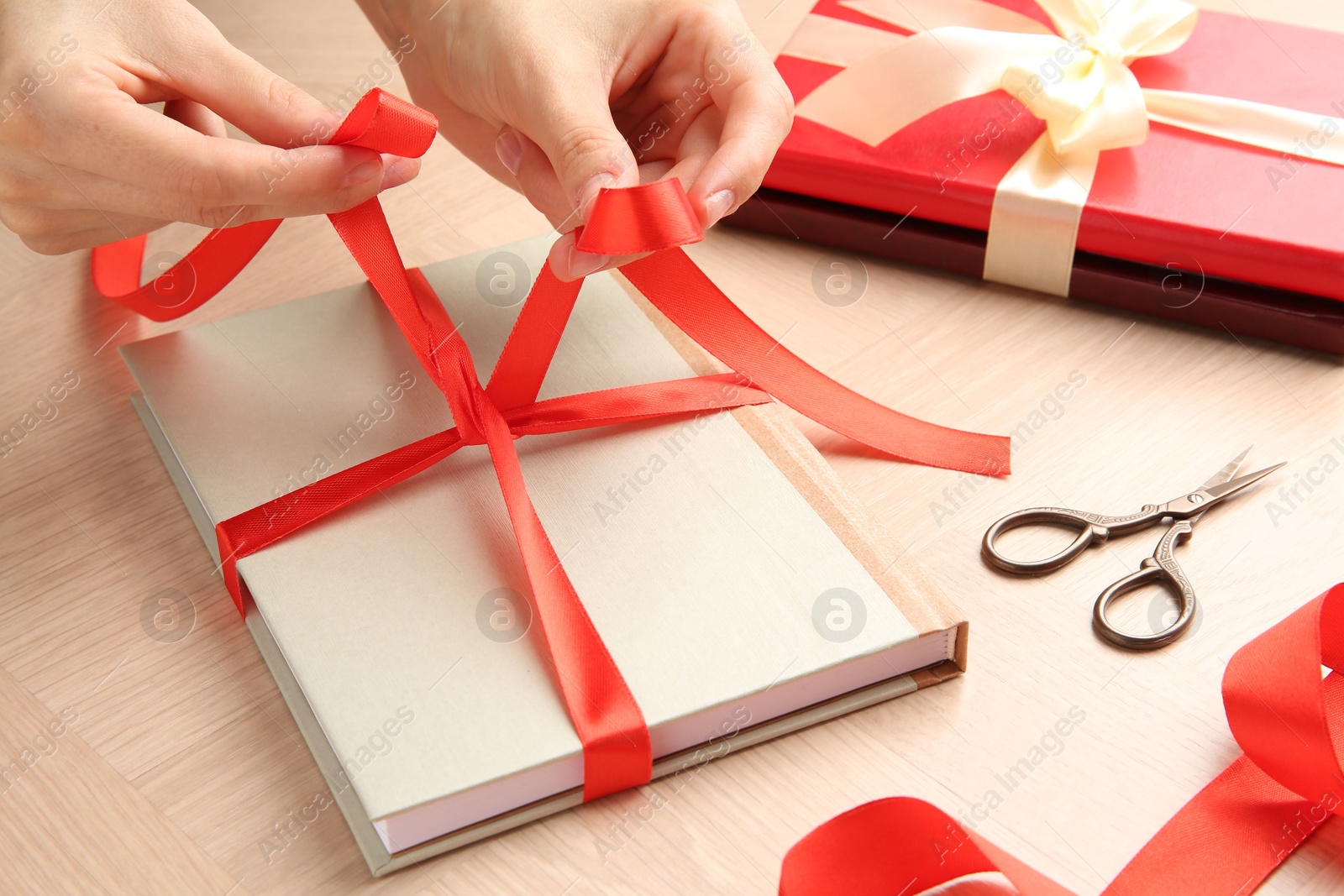 Photo of Woman tying ribbon on book at wooden table, closeup. Preparing gift