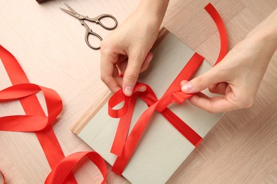 Woman tying ribbon on book at wooden table, top view. Preparing gift