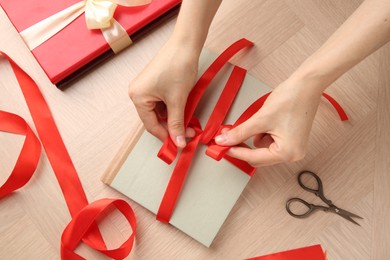 Woman tying ribbon on book at wooden table, top view. Preparing gift