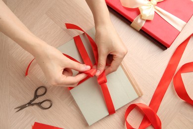 Photo of Woman tying ribbon on book at wooden table, top view. Preparing gift