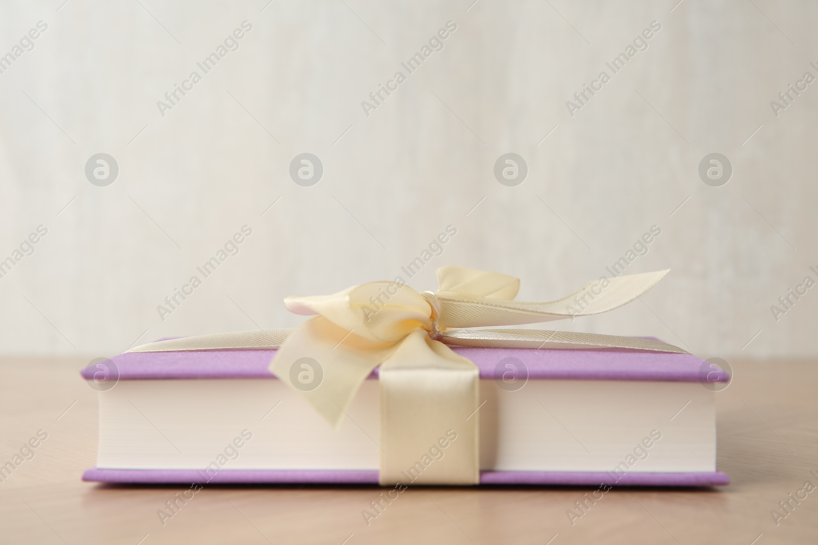 Photo of Hardcover book with ribbon as gift on wooden table