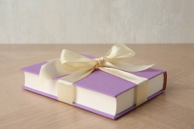 Photo of Hardcover book with ribbon as gift on wooden table