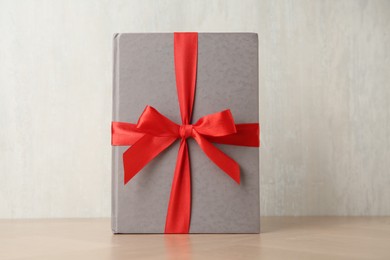 Photo of Hardcover book with ribbon as gift on wooden table