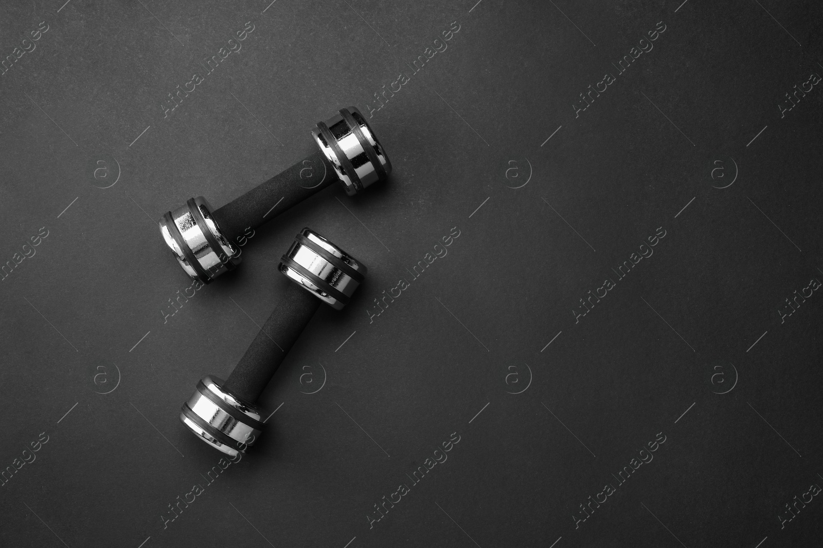 Photo of Two dumbbells on black background, top view. Space for text