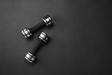 Photo of Two dumbbells on black background, top view. Space for text