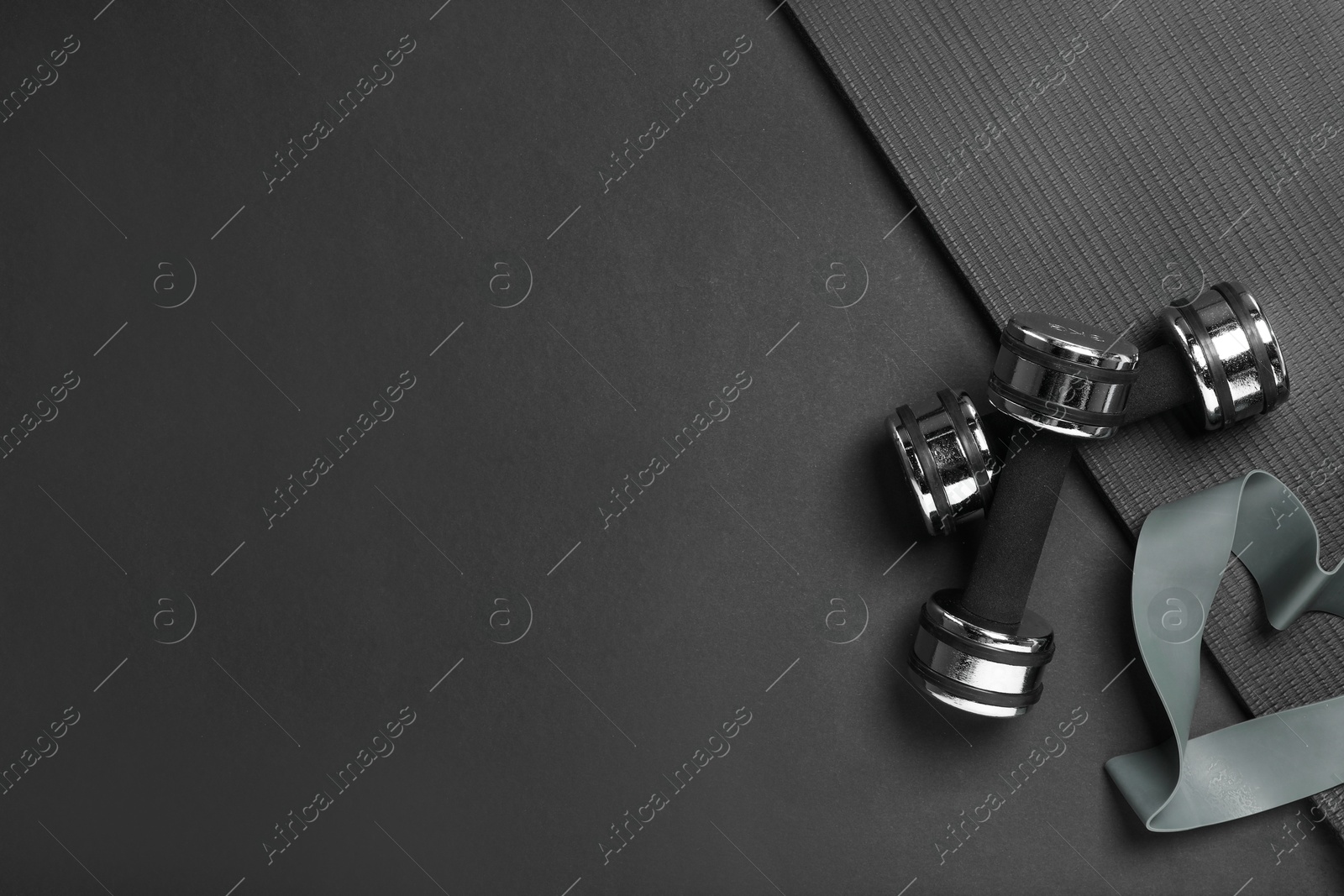 Photo of Dumbbells, yoga mat and fitness elastic band on black background, flat lay. Space for text