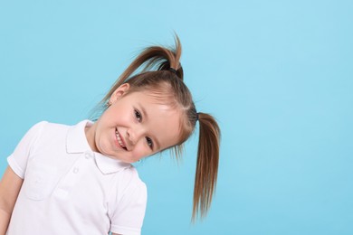 Photo of Portrait of happy little girl on light blue background, space for text