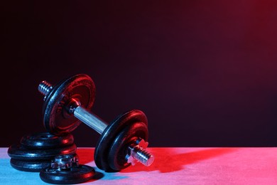 Photo of Barbell and parts of one on table in color lights. Space for text