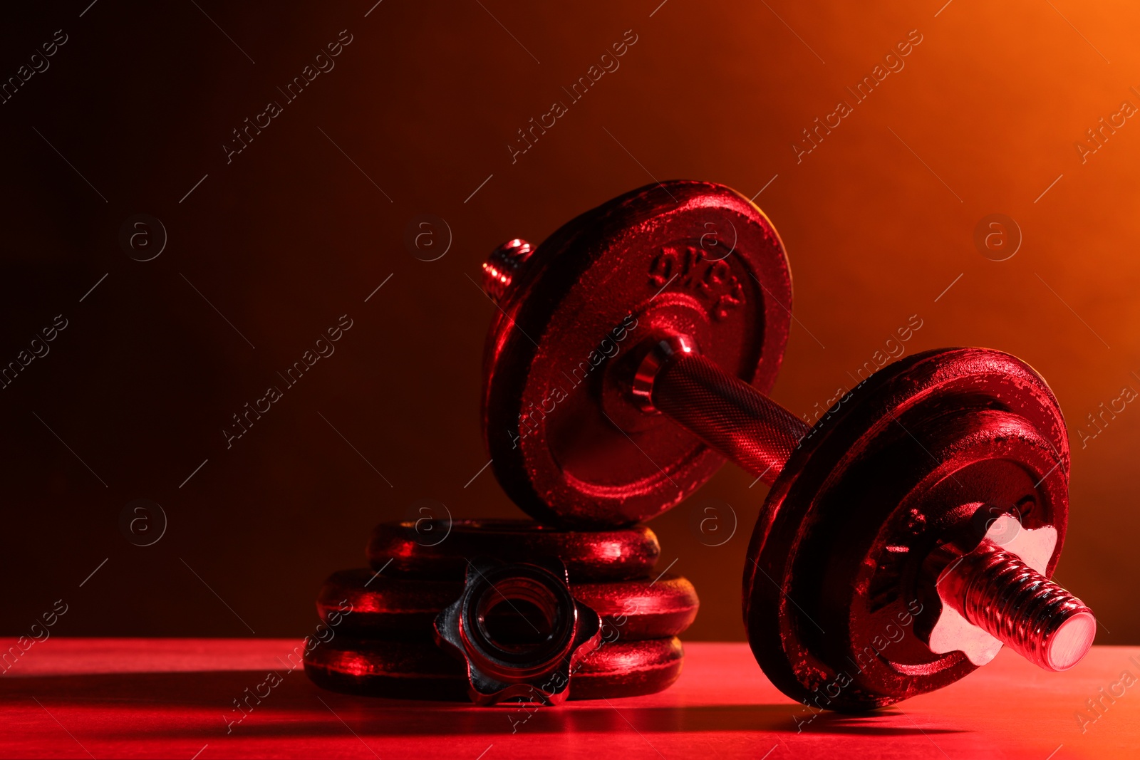 Photo of Barbell and parts of one on table in color lights. Space for text