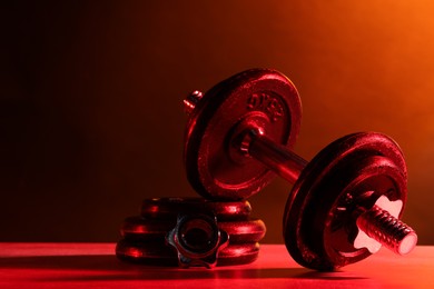 Photo of Barbell and parts of one on table in color lights. Space for text